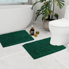 two green bath mats sitting on top of a bathroom floor next to a white toilet