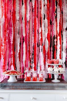 the dessert table is decorated with red, pink and white streamers hanging from the wall