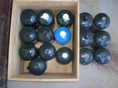 a wooden box filled with black vases on top of a cement floor next to a brick wall