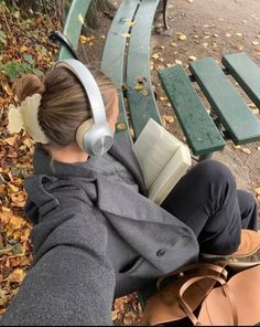 a woman with headphones sitting on a bench reading a book