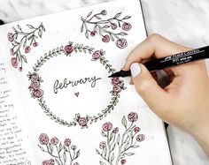 a woman's hand holding a marker and writing on a page with flowers around it