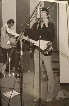 a man standing in front of a microphone while holding a guitar