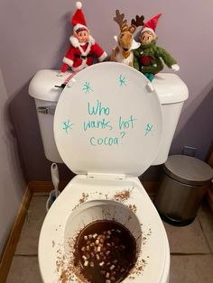 two elfs sitting on top of a toilet with cocoa in the bowl next to it