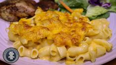 a white plate topped with macaroni and cheese covered in sauce next to salad