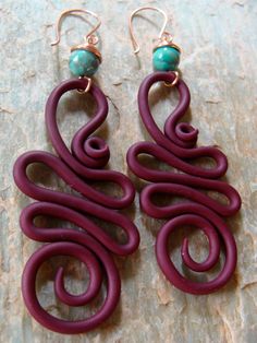 two pairs of purple and red earrings with turquoise beads on top of a piece of wood