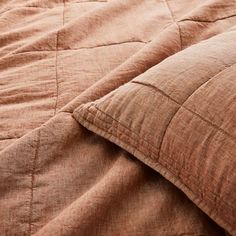 an unmade bed with brown linens and pillows on top of it, close up