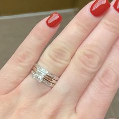 a woman's hand with two rings on it and red nail polish holding the ring