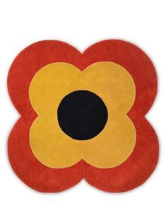 a red and yellow flower shaped rug on a white surface with black dots in the center