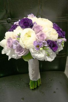 a bridal bouquet sitting on top of a black chair with purple and white flowers