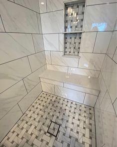 a bathroom with white and gray tile on the floor, shower head and shelf in the corner