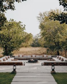 an outdoor seating area with couches and tables in the middle, surrounded by trees