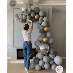 a woman standing in front of a giant balloon arch with silver and gold balloons on it