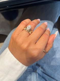 a woman's hand with two wedding rings on her left and the other hand holding an engagement ring