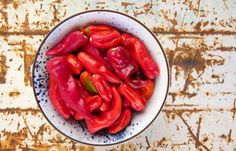 a white bowl filled with red peppers sitting on top of a wooden table next to a rusted wall