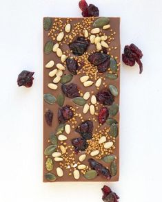 a chocolate bar topped with nuts and dried cranberries next to raisins