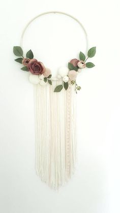 a white wall hanging with flowers and greenery on the top, along with long tassels