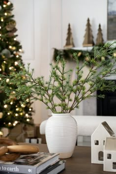 a small christmas tree in a white vase next to a book and some cookies on a table