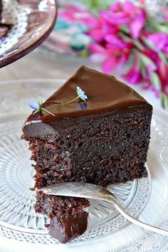 a piece of chocolate cake on a plate with a fork and flowers in the background