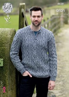 a man standing in front of a wooden fence wearing a gray sweater and black pants