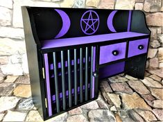 a purple and black cabinet with the moon on it's side, sitting in front of a stone wall