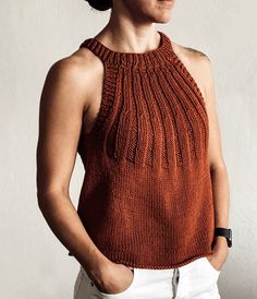 a woman standing with her hands in her pockets and looking off to the side, wearing an orange knitted top