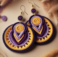 two purple and yellow earrings on top of a furnishing area next to feathers