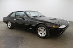 a black sports car is parked in a room with white walls and concrete flooring