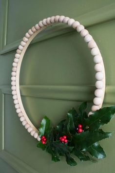 a wreath with holly and white beads hanging on the front door, next to a green door