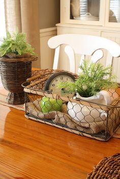 a wooden table topped with a basket filled with plants and an old clock sitting on top of it