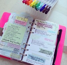 an open planner book with markers and writing on it next to a cup of pens