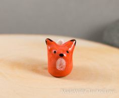 a small red fox figurine sitting on top of a wooden table next to a gray wall