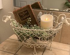 a candle and some books in a basket on the bathroom counter next to a mirror