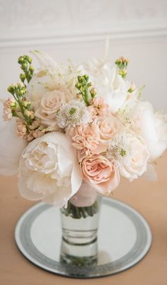 a vase filled with white and pink flowers on top of a wooden table next to a plate