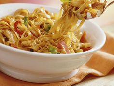 a white bowl filled with noodles and veggies on top of a wooden table