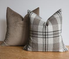 two pillows sitting on top of a wooden table next to each other, one in grey and white plaid