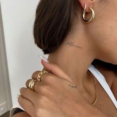 a woman with tattoos on her neck wearing gold hoop earrings and a white tank top