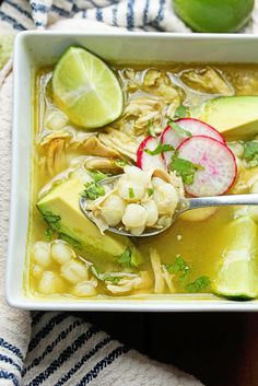 a white bowl filled with soup and garnished with avocado, radishes, cilantro, and lime