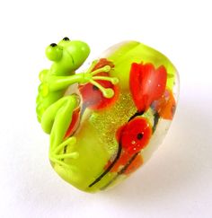 a glass frog figurine sitting on top of a flowered heart shaped object