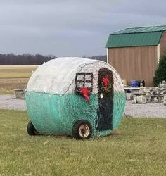 a trailer made out of hay sitting on top of a grass covered field next to a barn