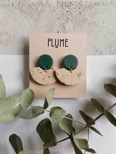 a pair of green and white earrings sitting on top of a card next to leaves