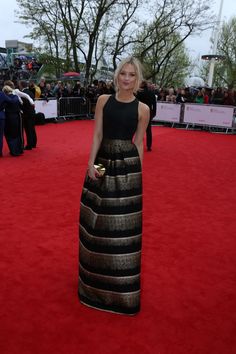 a woman in a black and gold dress standing on a red carpet at an event