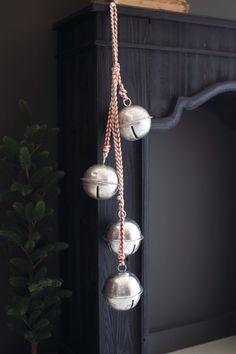 three silver bells hanging from the side of a fireplace with a christmas tree in front of it