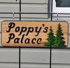 a wooden sign that says poppy's place hanging on the side of a house