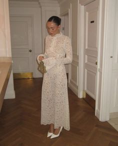 a woman in a long white dress is looking down at her purse while standing on the floor