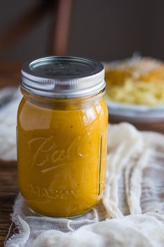 a jar filled with yellow liquid sitting on top of a wooden table next to another plate