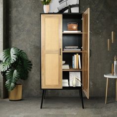 an open cabinet in the corner of a room next to a table and potted plant