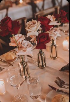 the table is set with wine glasses and roses in vases, candles and napkins