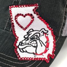 "Bulldogs Hat - Women's Georgia Trucker This women's bulldogs hat is a trucker hat with a embroidered patch in the shape of the State of Georgia. The hat is embellished with Swarovski Crystal Rhinestones. We use authentic red and white Swarovski rhinestones. A one size fits all gift for any Bulldogs girl on your list. The grey denim trucker is pictured, but you can choose from many hat styles. NEW - High ponytail option to pull your hair off of your neck. Great for those hot early fall games. 20 Georgia Outline, Georgia Hat, Rhinestone Hat, State Of Georgia, Fall Games, Hat Styles, Georgia State, High Ponytail, Early Fall