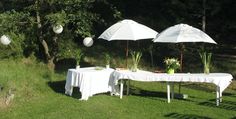 an outdoor dining table with two umbrellas over it and some flowers on the table