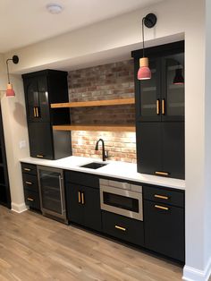 an empty kitchen with black cabinets and white counter tops, wood flooring and brick wall